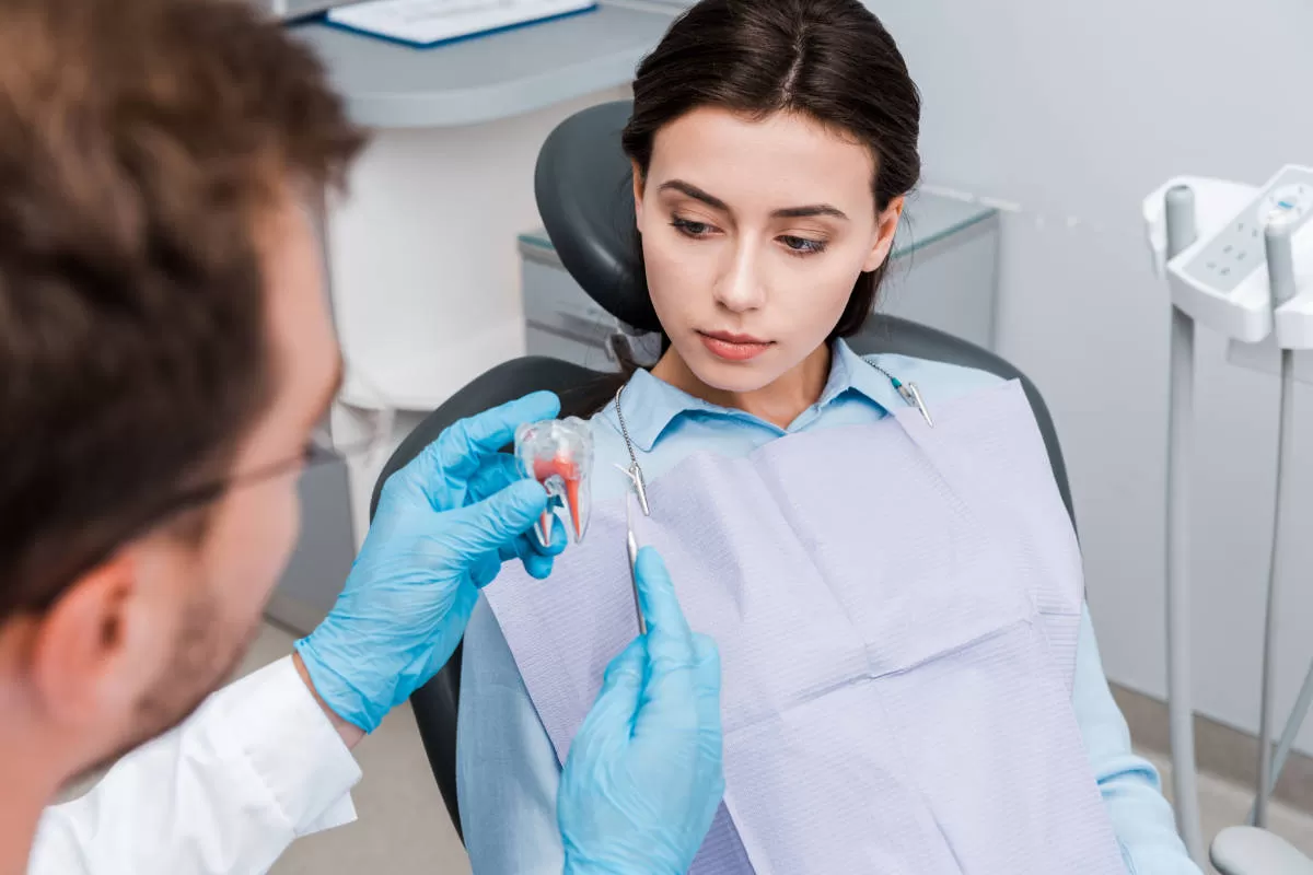 giovane donna dal dentista ascolta spiegazioni del dentista che le mostra il modellino di dente molare giovane donna dal dentista ascolta spiegazioni del dentista che le mostra il modellino di dente molare
