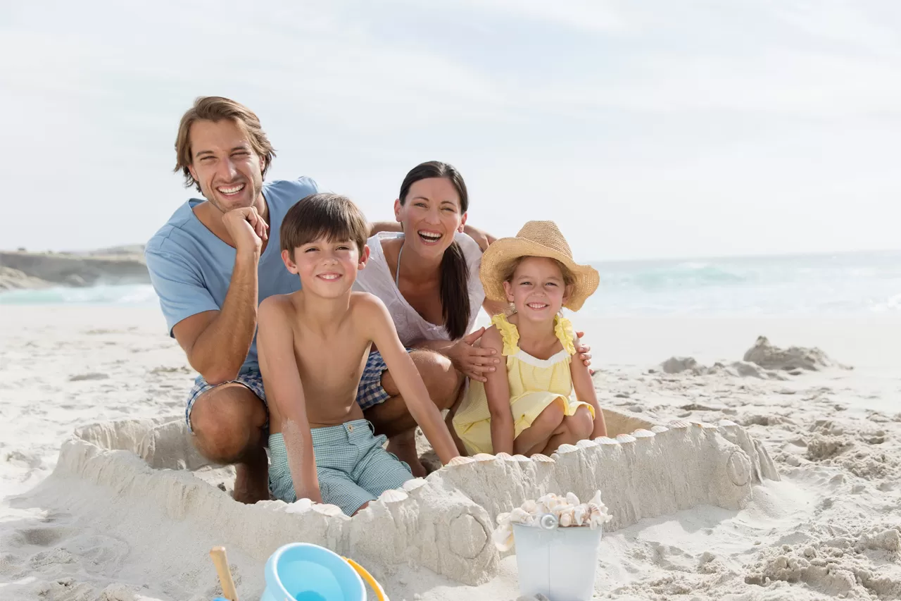 Famiglia felice in spiaggia che si gode le vacanze consapevole degli orari di agosto dei Centri Denti e Salute Group